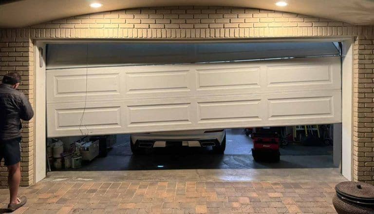 Man adjusting a malfunctioning garage door revealing a parked car inside.