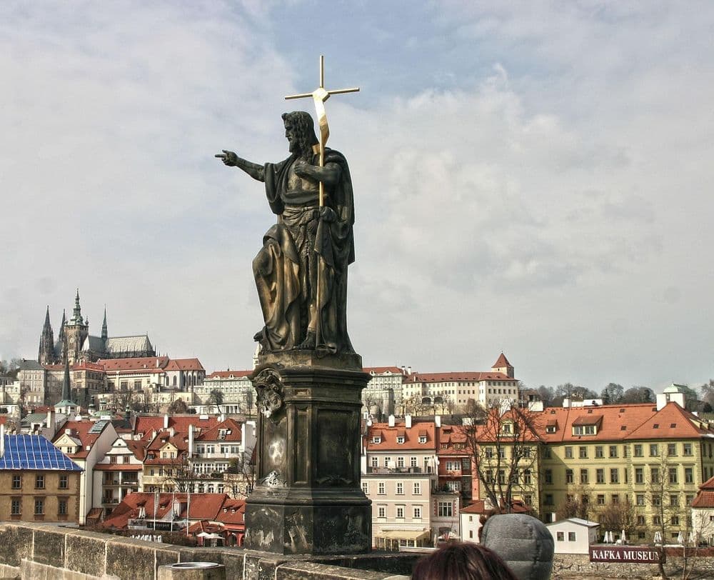 Statue of Saint John of Nepomuk with Prague's skyline in the background.